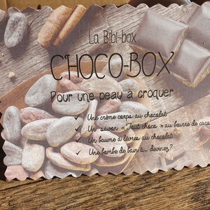 Puede incluir: Una tarjeta con el texto "La Bibi-box CHOCO-BOX Pour une peau &agrave; croquer" y una lista de productos de ba&ntilde;o y cuerpo con tem&aacute;tica de chocolate: "Une cr&egrave;me corps au chocolat", "Un savon "Tout choco" au beurre de cacao", "Un baume &agrave; l&egrave;vres au chocolat" y "Une bombe de bain &agrave;... devinez?"
