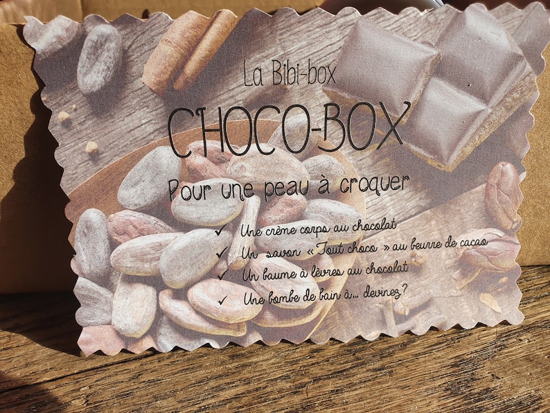 Puede incluir: Una tarjeta con el texto "La Bibi-box CHOCO-BOX Pour une peau &agrave; croquer" y una lista de productos de ba&ntilde;o y cuerpo con tem&aacute;tica de chocolate: "Une cr&egrave;me corps au chocolat", "Un savon "Tout choco" au beurre de cacao", "Un baume &agrave; l&egrave;vres au chocolat" y "Une bombe de bain &agrave;... devinez?"