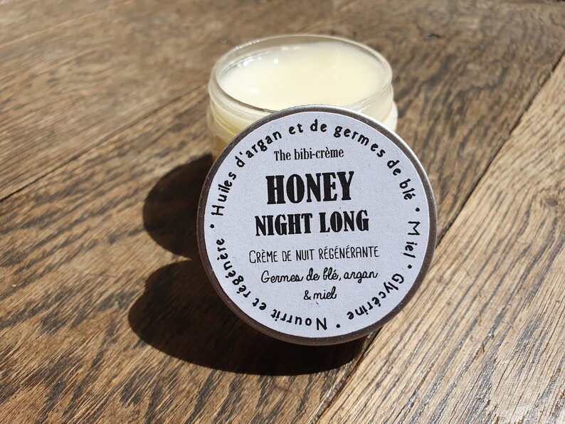 May include: A white jar with a silver lid labeled "Honey Night Long" with the text "The bibi-cr&egrave;me Cr&egrave;me de nuit r&eacute;g&eacute;n&eacute;rante Germes de bl&eacute;, argan & miel Huiles d'argan et de germes de bl&eacute;. Miel Glyc&eacute;rine et Nourrissante"