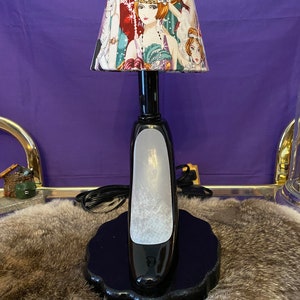 May include: A black high heel shoe shaped table lamp with a white frosted glass shade. The shade features a colorful print of women in flapper dresses.