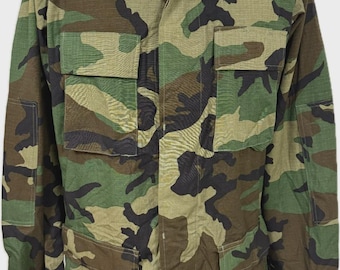 May include: Camouflage pattern jacket with four front pockets and button closures. The jacket features a classic military-style design with a green, brown, and black woodland camouflage print. The collar is a traditional fold-down style.