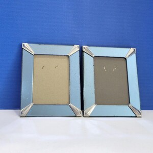 May include: Two matching light blue picture frames with silver accents. Each frame has a rectangular opening and a light brown backing. The frames are approximately 5 inches in height.