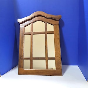 Puede incluir: Un espejo rectangular de madera con una parte superior decorativa. El espejo está dividido en secciones por marcos de madera. La madera tiene un tono marrón cálido. El espejo está diseñado para montarse en una pared.