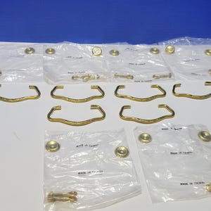 May include: A set of ten gold-toned cabinet pulls with a decorative design. The pulls are packaged in clear plastic bags with the text "Made in Taiwan".