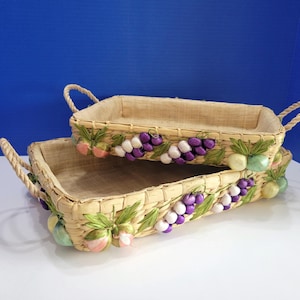 May include: Two rectangular woven baskets with rope handles. The baskets are decorated with clusters of purple and white grapes, green leaves, and pastel-colored fruit accents. The baskets are stacked on top of each other.