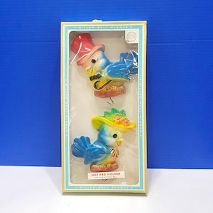May include: A boxed set of two vintage ceramic bird wall plaques. The birds are blue with red, yellow, and green accents. One bird wears a top hat, the other a hat with a floral design. The box reads "Miller Wall Plaque" and "Hot Pad Holder".