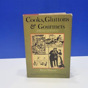 May include: A vintage cookbook titled "Cooks, Gluttons & Gourmets, A History of Cookery" by Betty Wason. The book has a green cover with illustrations and text in black and red. The book is standing upright.