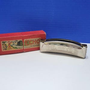 May include: A silver harmonica with the text "M. Hohner" and decorative etchings, next to a red box with the word "ECHO" and a landscape illustration. The harmonica is a musical instrument.