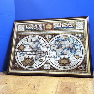 Op de afbeelding: Ingelijste vintage wereldkaart met een donkerbruine houten lijst. De kaart toont twee cirkelvormige wereldkaarten met gedetailleerde illustraties en tekst. De tekst bovenaan luidt "A NEW AND ACCURATE MAP OF THE WORLD."