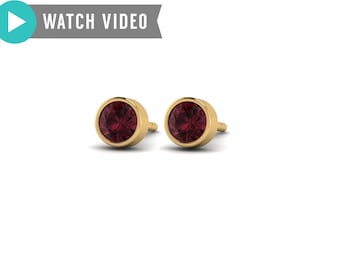 May include: A pair of gold stud earrings with a round, red gemstone in the center.