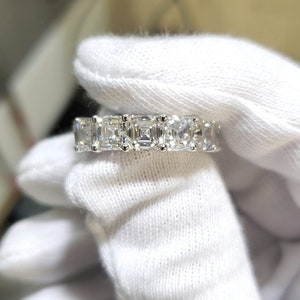 May include: A silver band ring with a row of square-shaped diamonds.