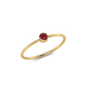 Puede incluir: Un anillo de banda de oro simple con una pequeña piedra preciosa redonda de color rojo.