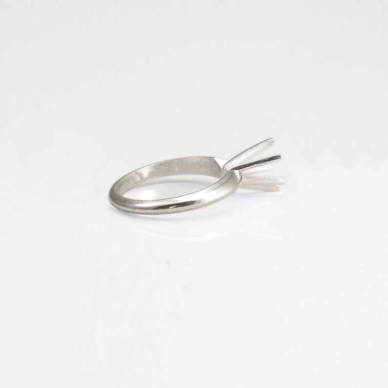 May include: A silver ring setting with a prong setting for a solitaire diamond.