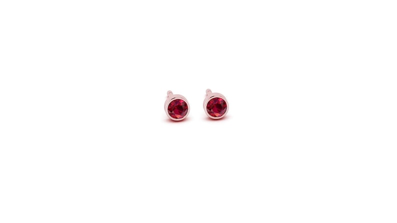 May include: A pair of small, round stud earrings with red gemstones set in a silver tone metal.