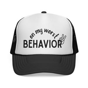 Può includere: Cappellino da camionista bianco e nero con la scritta nera "on my worst behavior" sopra la parola "BEHAVIOR". Un segno di pace è accanto alla parola "BEHAVIOR". Il cappellino ha una visiera nera e un retro in rete.