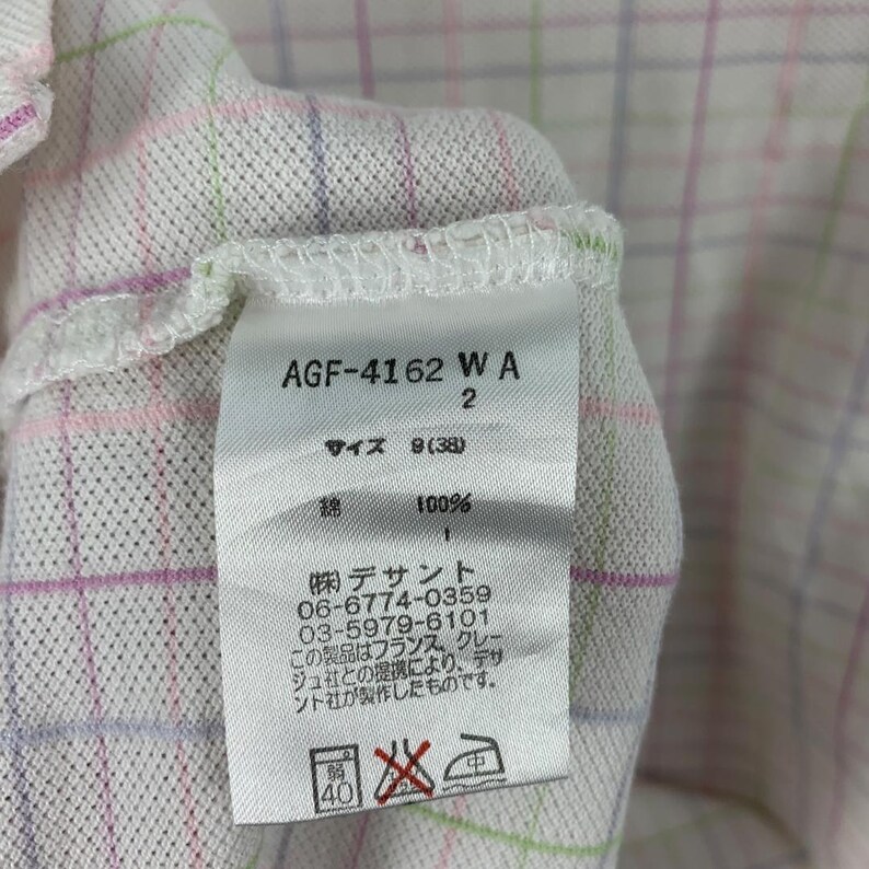 May include: Close-up of a white fabric tag with text and numbers. The tag reads "AGF-4162 WA 2" and "サイズ 8(38)". The tag also includes Japanese text and washing instructions.