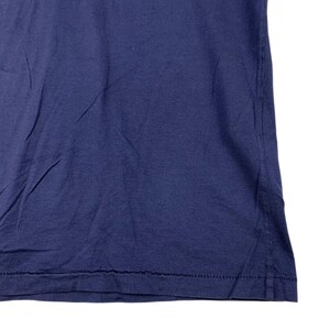 May include: A solid navy blue t-shirt featuring a standard crew neckline and short sleeves. The fabric has a smooth texture with visible stitching along the bottom hemline, showcasing a classic construction and a deep, uniform colour throughout.