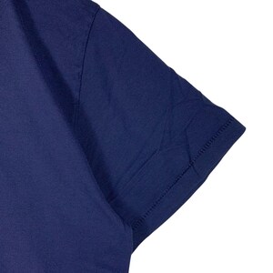 May include: A solid dark navy blue short-sleeved t-shirt featuring a smooth fabric texture, a clean hemmed sleeve edge, and visible stitching along the shoulder seam. The garment is presented against a plain white background, highlighting the deep blue colour.