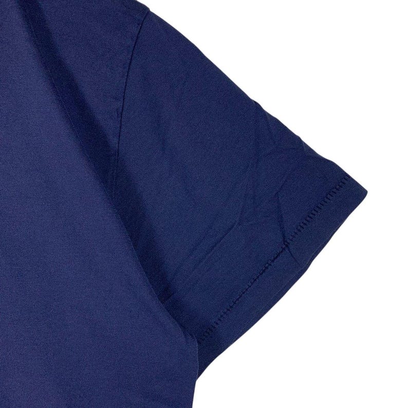 May include: A solid dark navy blue short-sleeved t-shirt featuring a smooth fabric texture, a clean hemmed sleeve edge, and visible stitching along the shoulder seam. The garment is presented against a plain white background, highlighting the deep blue colour.