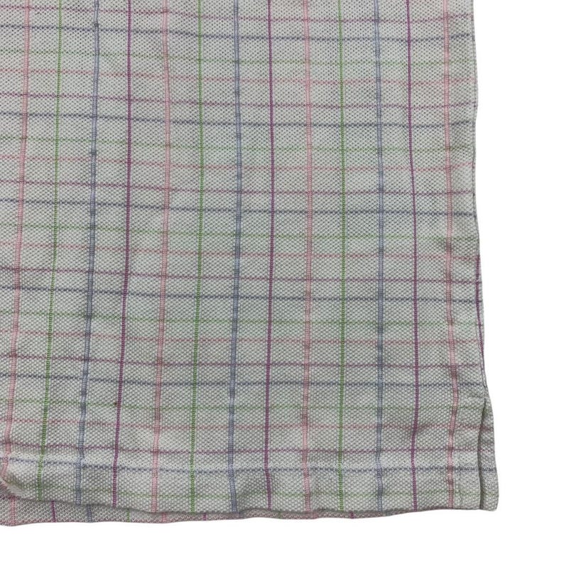 May include: Close-up of a white fabric with a plaid pattern. The plaid design features thin lines in pink, green, purple, and blue, creating a grid-like appearance. The fabric has a textured surface.
