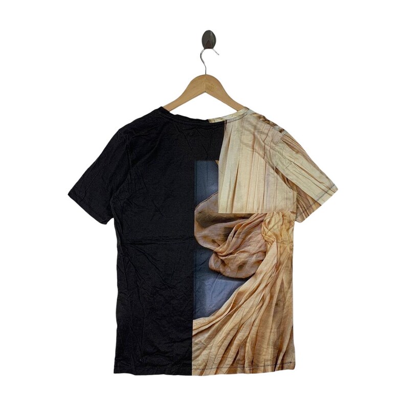 May include: A short-sleeve t-shirt featuring a split design. The left side is solid black, while the right side displays a photographic print of draped, light beige fabric with vertical lines and soft folds, creating a high-contrast visual effect.
