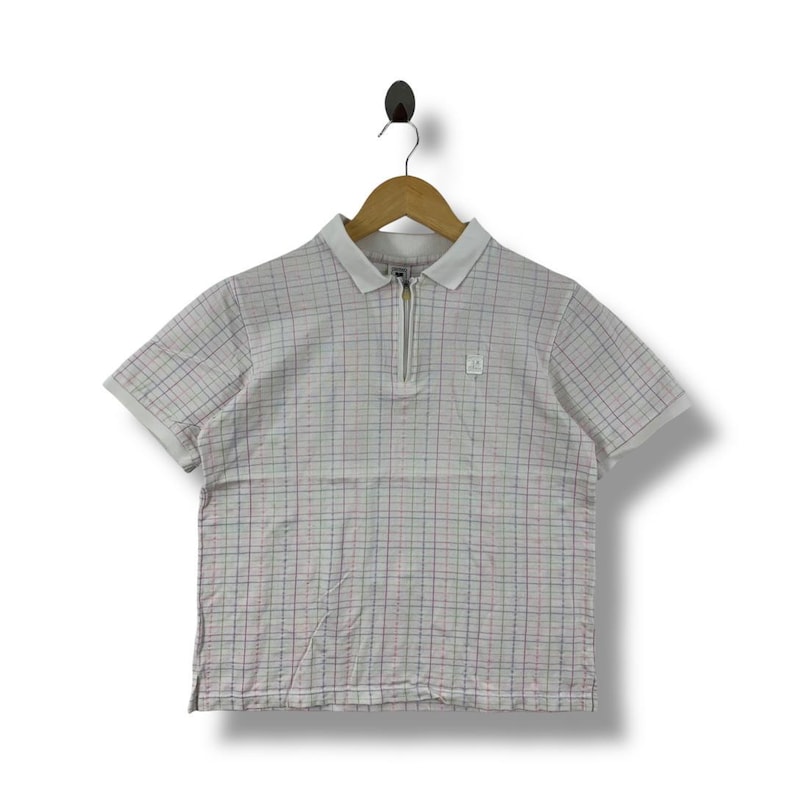 May include: A short-sleeved polo shirt with a white collar and a quarter-length zipper. The shirt features a plaid pattern in red, blue, and green on a white background. A small logo is visible on the chest.