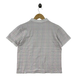 May include: White polo shirt with a plaid pattern in red, blue, and green. The shirt has short sleeves and a white collar. The shirt is hanging on a wooden hanger.