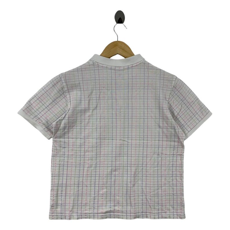 May include: White polo shirt with a plaid pattern in red, blue, and green. The shirt has short sleeves and a white collar. The shirt is hanging on a wooden hanger.