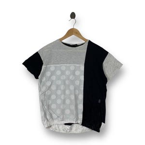 May include: A short-sleeve t-shirt featuring a color-blocked design with a heather gray upper section, a white lower section with large light gray polka dots, and a solid black vertical panel on the right side, finished with a gathered elastic hem.