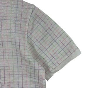 May include: A white polo shirt with a multicolored plaid pattern. The short-sleeved shirt has a classic collar and a textured fabric. The plaid design features lines of pink, green, blue, and purple.