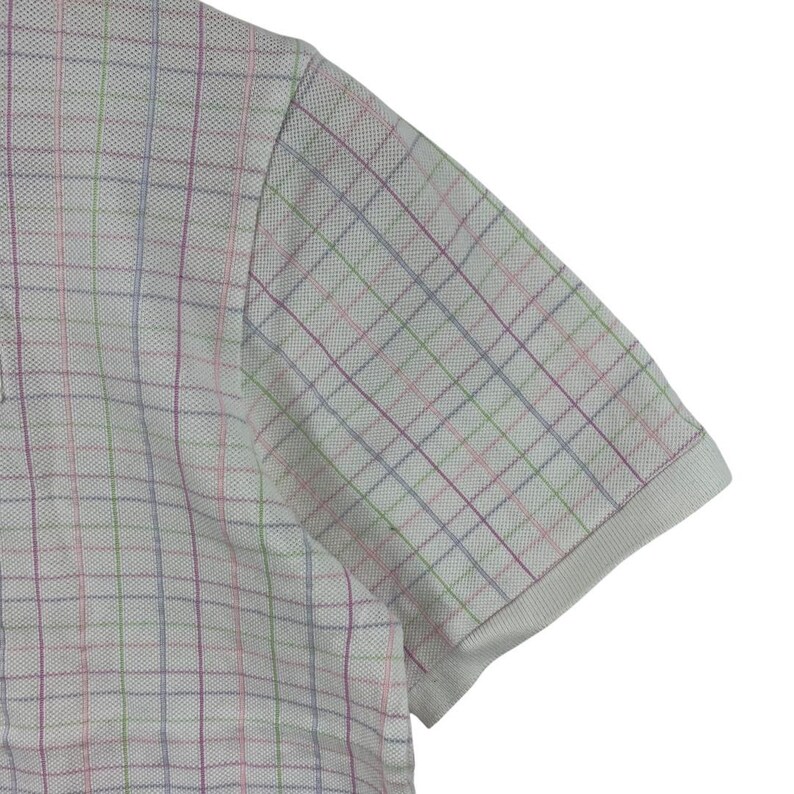 May include: A white polo shirt with a multicolored plaid pattern. The short-sleeved shirt has a classic collar and a textured fabric. The plaid design features lines of pink, green, blue, and purple.
