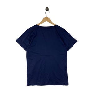 May include: A solid navy blue short-sleeved t-shirt with a crew neckline. The garment is displayed on a wooden hanger, showing a plain back view with a simple hemline on the sleeves and the bottom edge of the shirt, featuring a clean design.