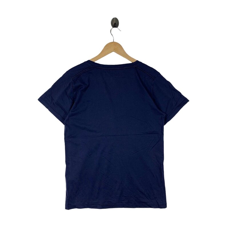 May include: A solid navy blue short-sleeved t-shirt with a crew neckline. The garment is displayed on a wooden hanger, showing a plain back view with a simple hemline on the sleeves and the bottom edge of the shirt, featuring a clean design.
