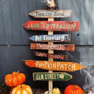 May include: A wooden signpost with multiple directional arrows pointing to various Halloween destinations, including "Twilight Zone", "Haunted Mansion", "Pet Cemetery", "Transylvania", "Sleepy Hollow", "Pumpkin Patch", and "Elm Street". The signpost is decorated with a skull and spider, and there are pumpkins on the ground.