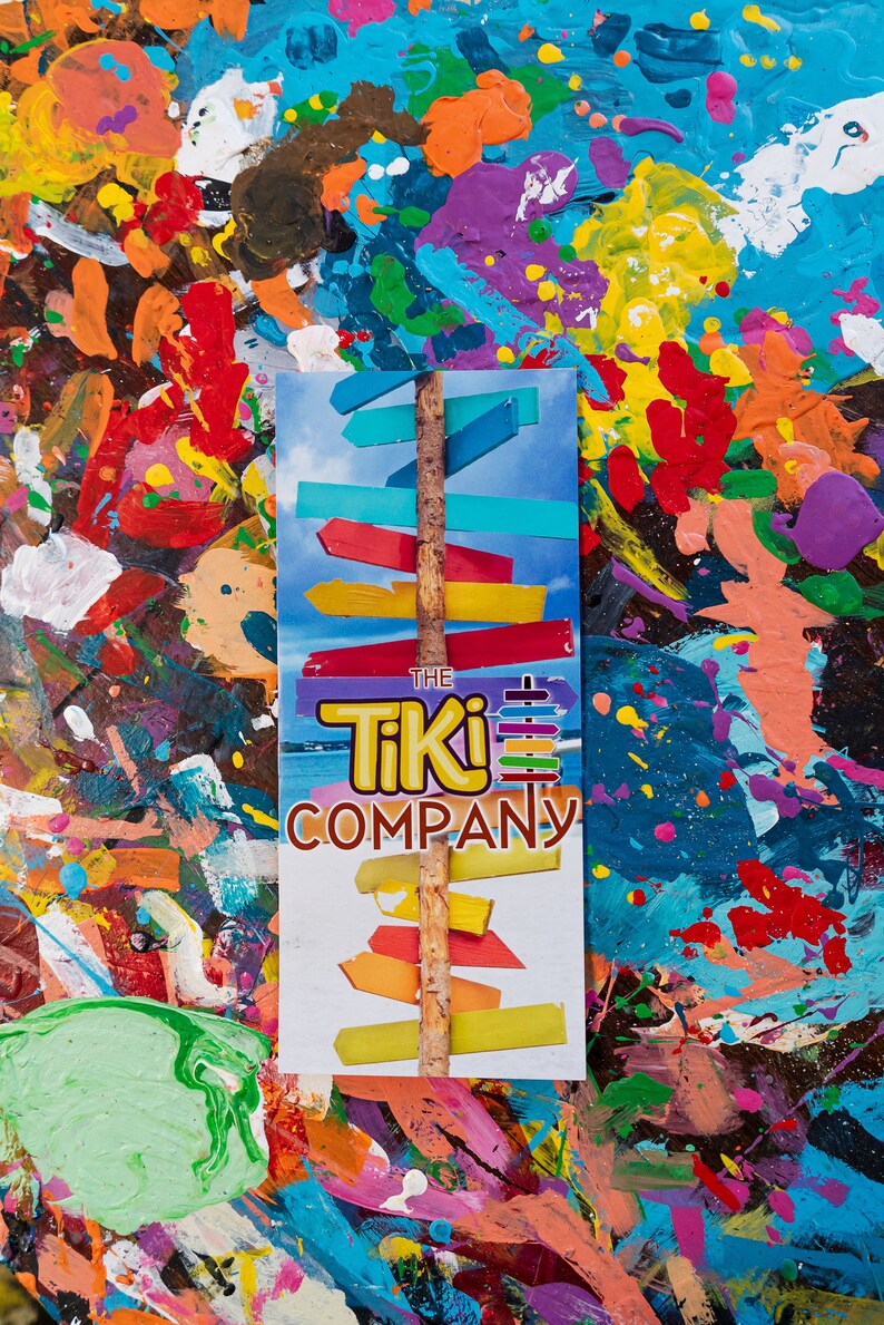 May include: A colourful, abstract background with a white sign that says "The Tiki Company". The sign features a wooden stick with multiple colourful wooden arrows pointing in different directions.