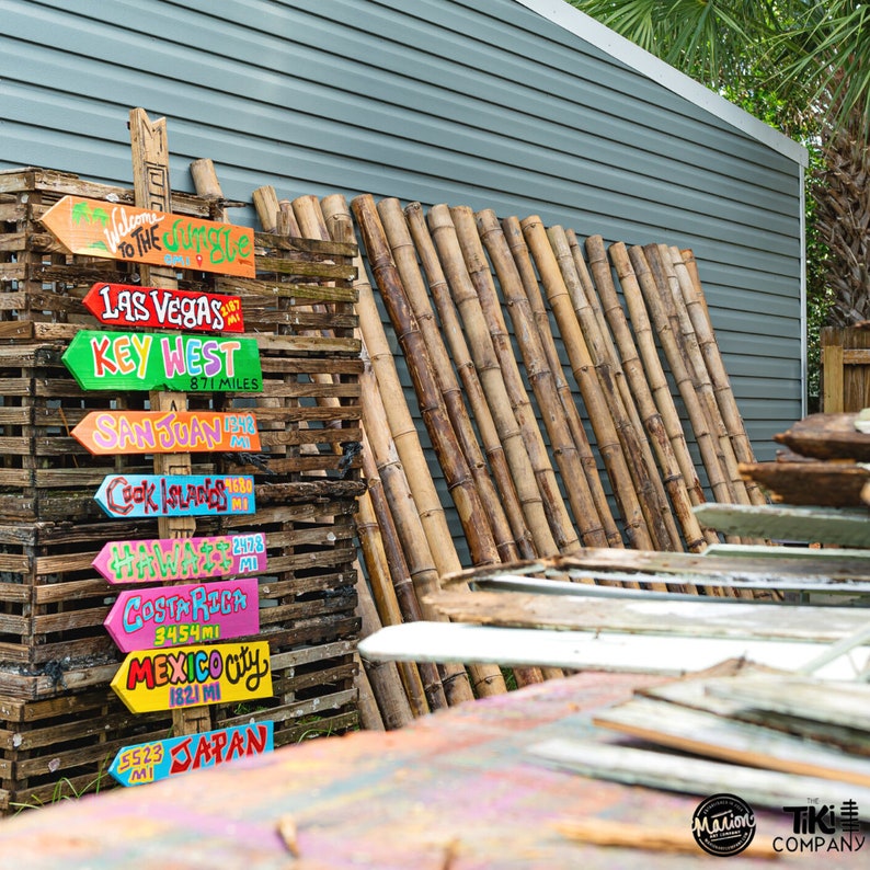 Pu&ograve; includere: Un cartello di legno con frecce colorate che puntano in direzioni diverse. Ogni freccia ha una destinazione scritta su di essa, come "Las Vegas", "Key West" e "Giappone". Il cartello &egrave; fatto di legno invecchiato e ha un aspetto rustico. Le frecce sono dipinte in colori vivaci e hanno un aspetto fantasioso.