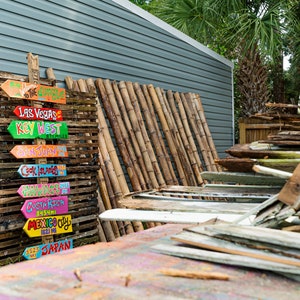 May include: A stack of wooden crates with colourful painted wooden signs pointing to different destinations, including Las Vegas, Key West, San Juan, Cook Islands, Costa Rica, Mexico City, and Japan.