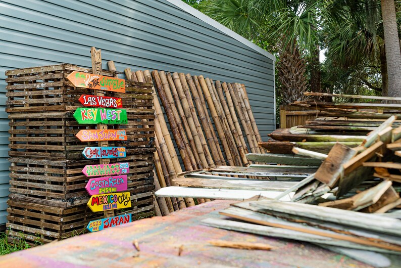 May include: A stack of wooden crates with colourful painted wooden signs pointing to different destinations, including Las Vegas, Key West, San Juan, Cook Islands, Costa Rica, Mexico City, and Japan.