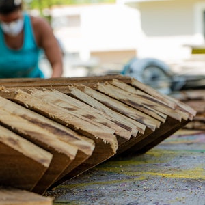 May include: A close-up of a stack of wooden planks, cut at an angle, with a blurred image of a person in the background.