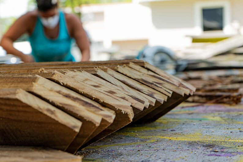 May include: A close-up of a stack of wooden planks, cut at an angle, with a blurred image of a person in the background.