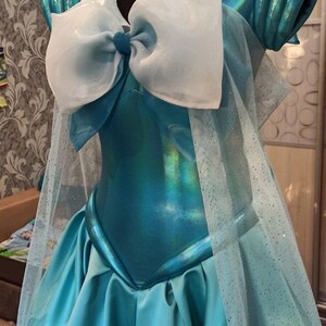 May include: A blue and white cosplay costume with a large white bow and a sheer overlay. The costume is made of a shiny fabric and has a fitted bodice and a full skirt.