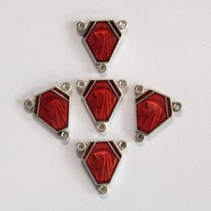 May include: Five silver-toned rosary centerpieces with a red enamel design. Each centerpiece is a pentagon shape with three holes for connecting to other rosary beads. The red enamel features a religious figure.