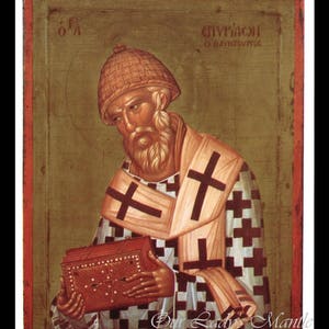 May include: An icon depicting a bearded man wearing a checkered robe and a brown hat. He is holding a book in his left hand. The icon is painted on a wooden panel and has a gold frame. The text "Ο' ΑΓΙΟΣ ΘΕΟΔΩΡΟΣ" is written in Greek at the top of the icon.