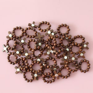 May include: A pile of brown wooden bracelets with silver crosses. Each bracelet has a circle of brown beads with a silver cross charm.