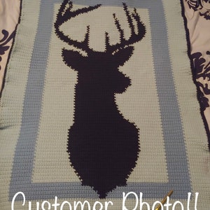 May include: A crocheted blanket with a blue and green border and a black silhouette of a deer with antlers in the center. The blanket is on a bed with a floral pattern. The text "Customer Photo!!" is at the bottom of the image.