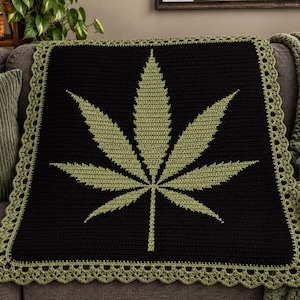 May include: A rectangular crochet blanket featuring a large, centered light green cannabis leaf motif against a solid black background. The blanket is finished with a decorative, scalloped light green crochet border along all four edges.