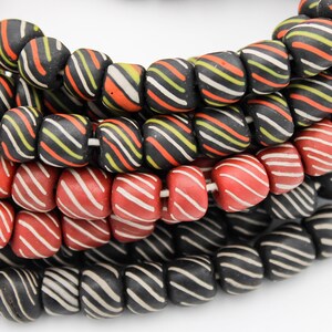 May include: Close-up of several strands of colorful, square-shaped beads. The beads are black, red, and orange, with white and yellow stripes. The beads are strung together, creating a textured and vibrant pattern.
