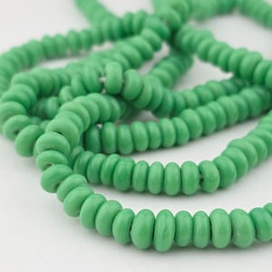 Peut inclure: Gros plan sur plusieurs brins de perles rondes vert clair. Les perles sont de taille et de forme uniformes, avec une finition légèrement mate. Les brins sont entrelacés, créant un effet de superposition.