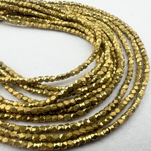 May include: Close-up of multiple strands of small, faceted, golden-colored beads. The beads have a metallic sheen and are arranged in a layered pattern, creating a textured and visually appealing display. Ideal for jewelry making or craft projects.