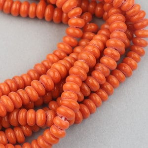 Peut inclure: Un brin de perles en céramique orange, chaque perle est en forme de beignet avec une finition lisse et brillante.